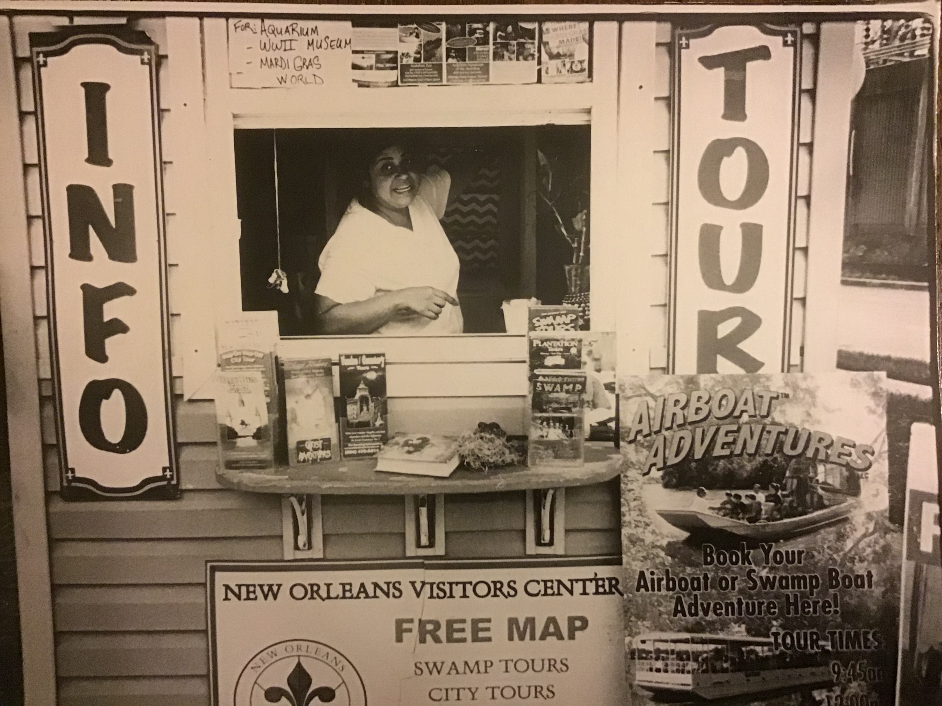 A sepia toned photograph featuring a woman inside a tour operators stand and signs with "info" and "tour" on either side of her.