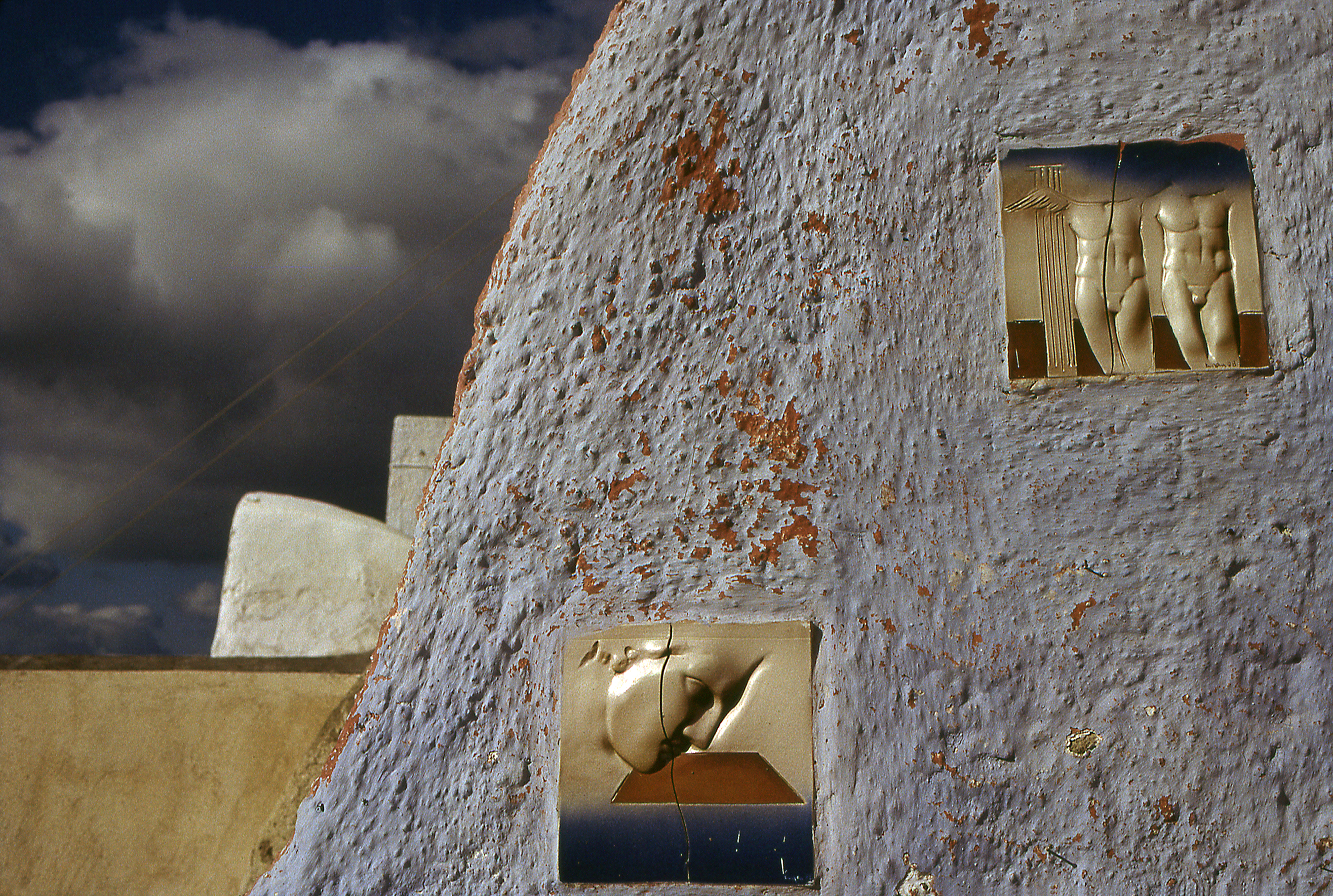 "Art Tiles" Two ceramic tiles, one with a face, the other two nude classical greek males figure. The tiles attached to the side a a stucco house.
