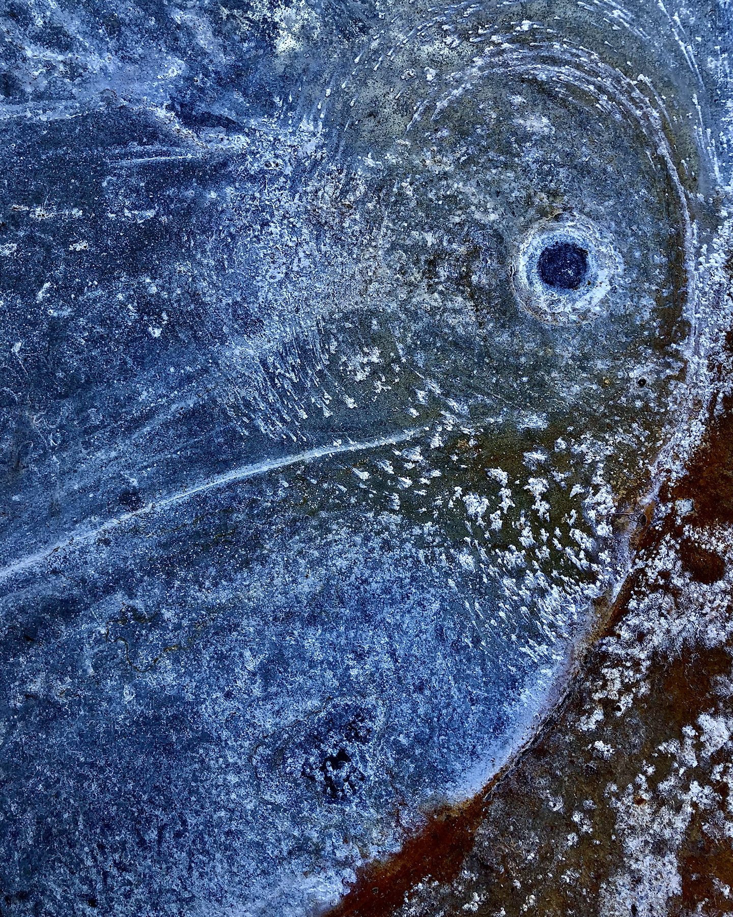 An abstract photo of a discarder water heater pan that is mostly blue with hints of white and brown, and resembles a face in the form of storm pattern radar.